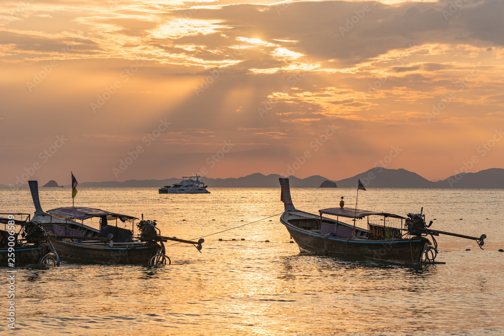 Several local thai longtail motor boats under golden sun rays in the sea water at orange sunset in Ao Nang in Krabi