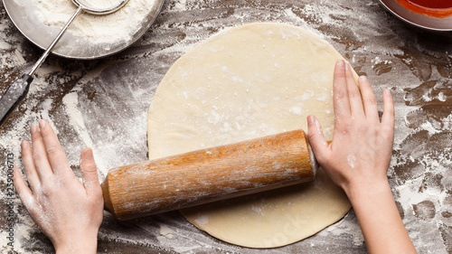 Woman preparing dough for pizza on table, top view