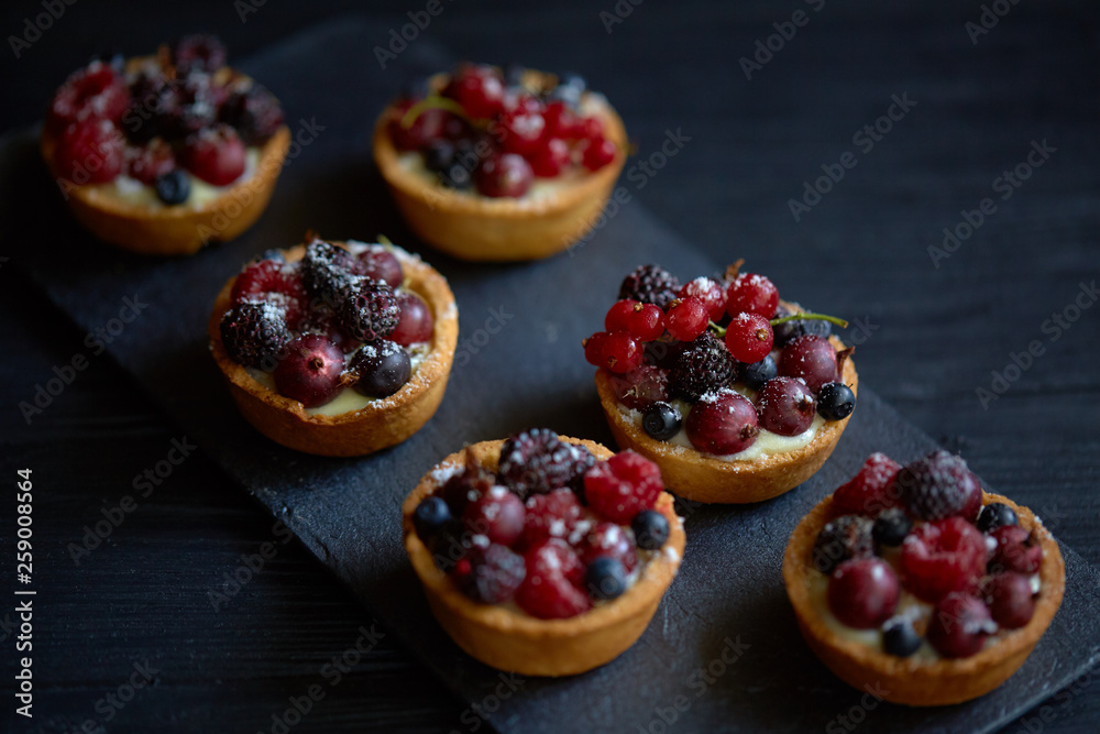 Sweet tarts with vanilla custard and berries on black wooden background