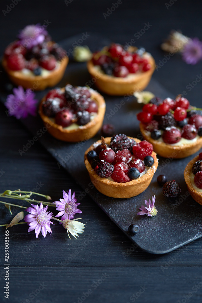 Sweet tarts with vanilla custard and berries on black wooden background