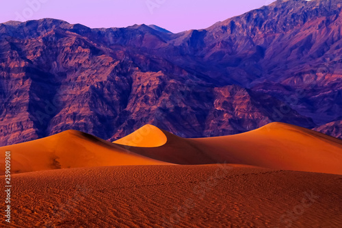 Vivid colors of sunset in Death Valley National Park with purple mountains behind sand dunes.