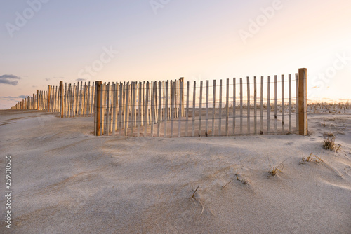 Sand Dune, Fence, and Sky Glowing at Sunrise in Cape Cod. © junej