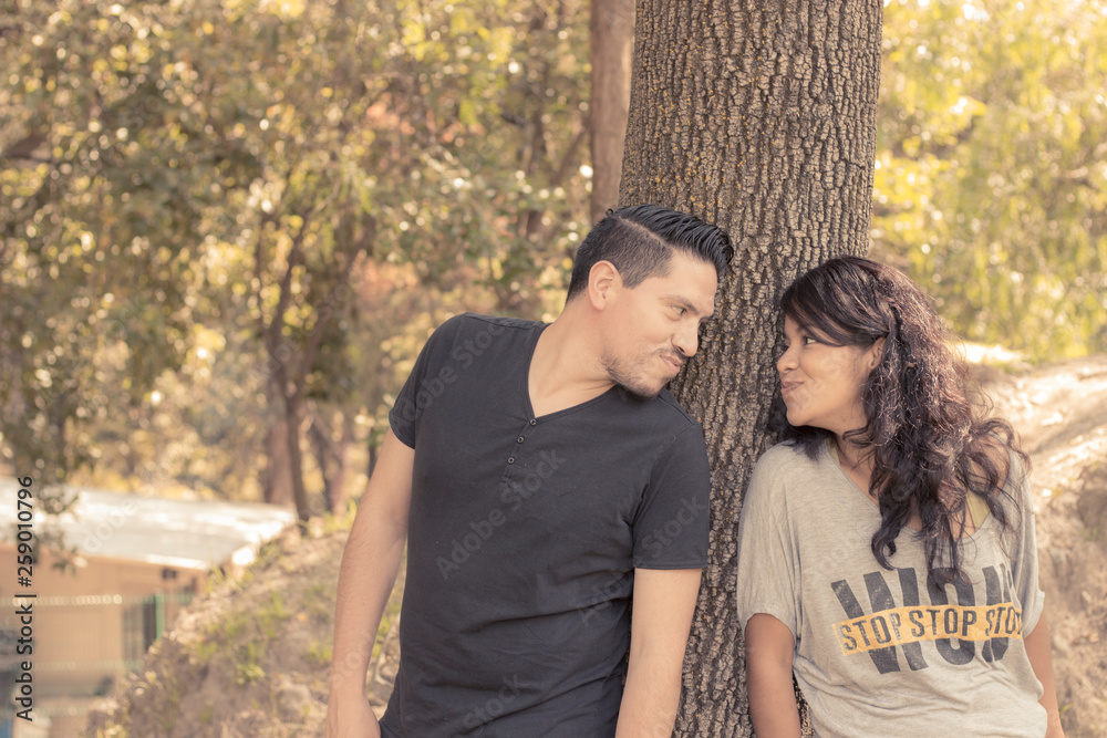 Fototapeta premium pareja jugando y coqueteando a traves de un arbol en medio del bosque, par de novios enamorados, couple playing and flirting through a tree in the middle of the forest, couple in love