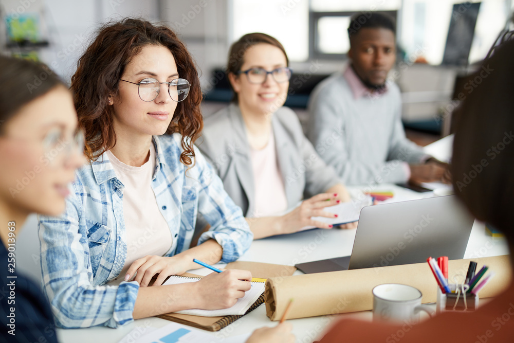 Group of contemporary people working in meeting focus on curly haired young woman in foreground, copy space Group of contemporary people working in meeting focus on curly haired young woman in foreground, copy space