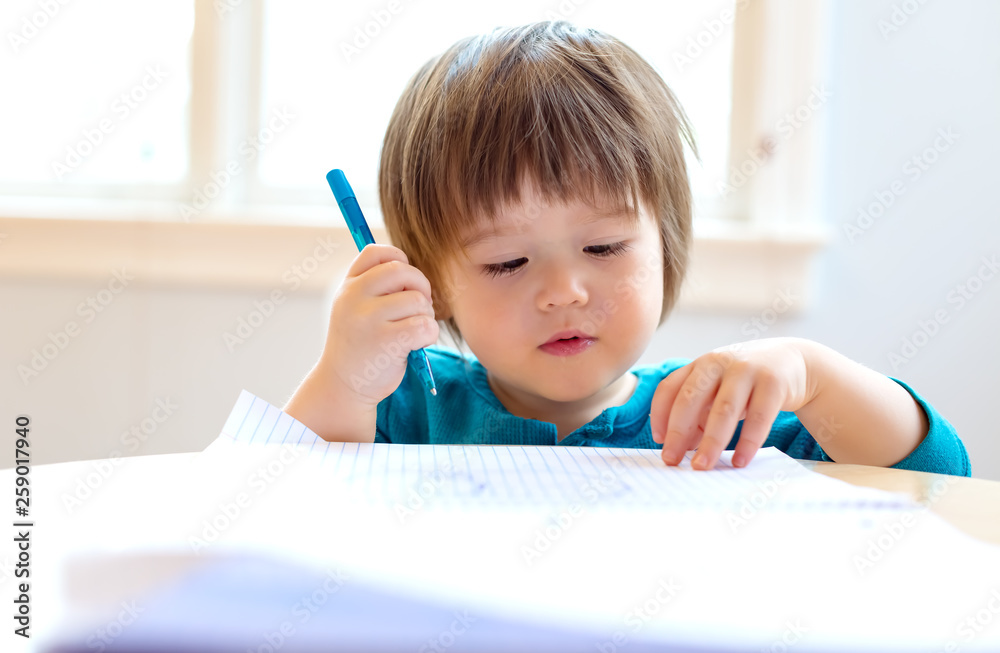 Toddler boy drawing with pen and paper at his desk Toddler boy drawing with pen and paper at his desk