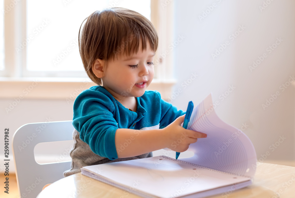 Toddler boy drawing with pen and paper at his desk Toddler boy drawing with pen and paper at his desk