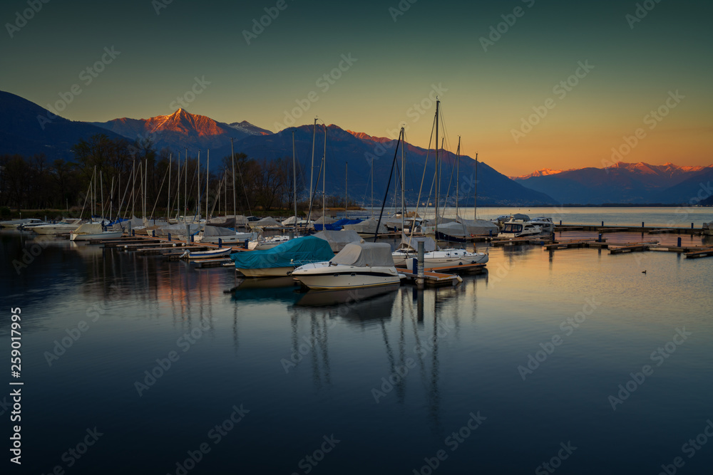 Dark green and yellow sunset with boats in the port of Ascona, Switzerland