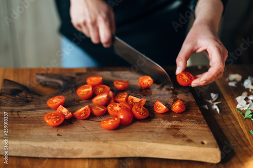 Chef chopping cherry tomatoes with knife on a wooden board