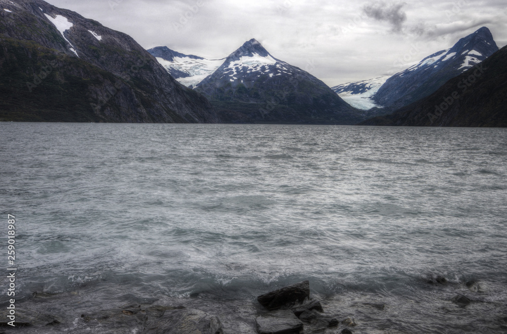 Glaciers lay around the mountains of Alaska along side a lake.