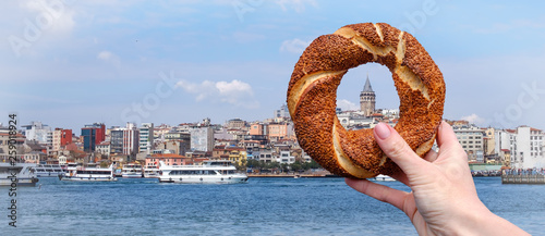 Traditional Turkish bagel simit in a female hand on the background of the panorama of Istanbul and the Galata Tower, horizontal banner