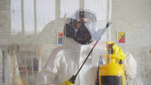 Close up exterminator in overalls carries out surface treatment by means of a spray