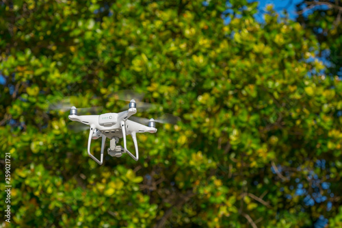 Drone in flight, green trees in the background, selective focus on the drone.