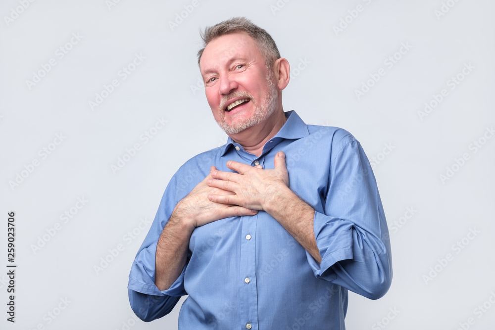 Fotografie Man smiles happily, keeps hands on chest