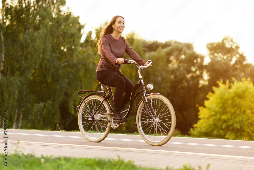 Young attractive woman riding through the park after work. Beautiful lady cycling during sunset. Bike as a trendy transport. Healthy outdoors activity on a warm summer day. Bicycle trend in the city. Young attractive woman riding through the park after work. Beautiful lady cycling during sunset. Bike as a trendy transport. Healthy outdoors activity on a warm summer day. Bicycle trend in the city.