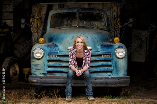 Attractive young woman sitting on the bumper of an old truck photo