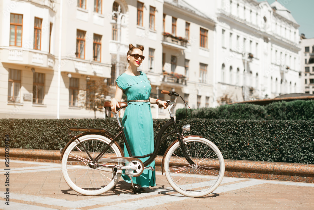 Fototapeta premium Young attractive woman riding through the park after work. Beautiful lady cycling during sunset. Bike as a trendy transport. Healthy outdoors activity on a warm summer day. Bicycle trend in the city.