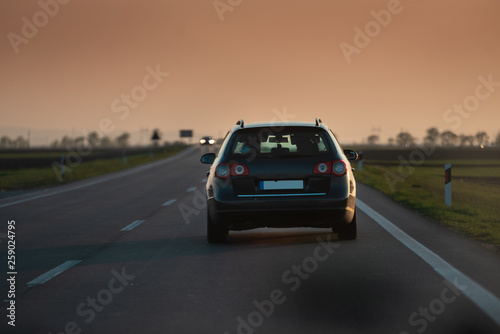 a black car drives towards the sunset