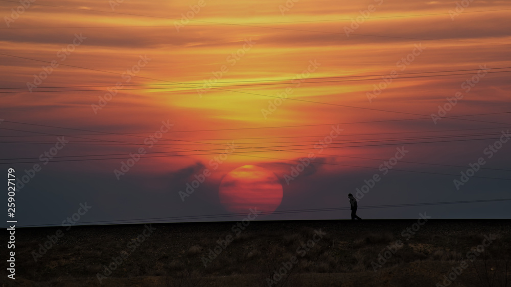Silhouette of a lone passerby on the background of power lines and the setting sun