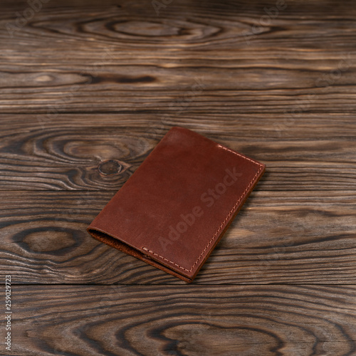 Ginger color handmade leather passport cover on wooden textured background. Businessman`s accessory.