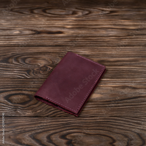 Purple color handmade leather passport cover on wooden textured background. Businessman`s accessory.
