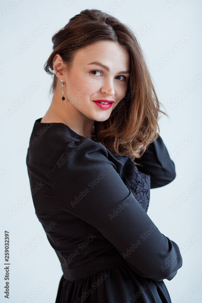 beautiful girl with red lipstick and in a black dress flirts. She is standing against a gray background beautiful girl with red lipstick and in a black dress flirts. She is standing against a gray background