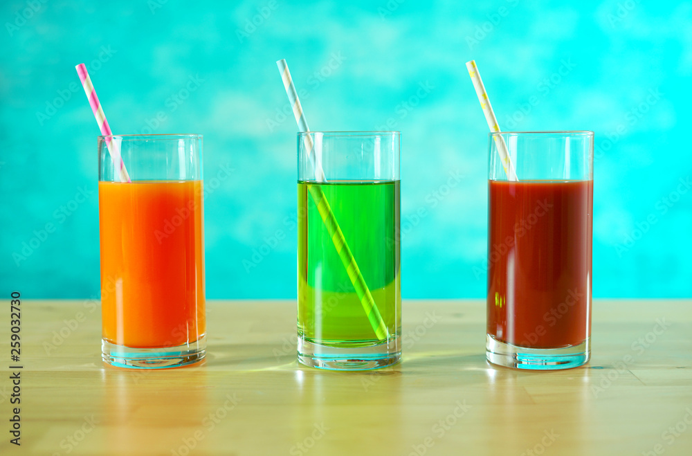 Fresh orange, apple and tomato juices in glasses with paper straws in bright table setting. Fresh orange, apple and tomato juices in glasses with paper straws in bright table setting.