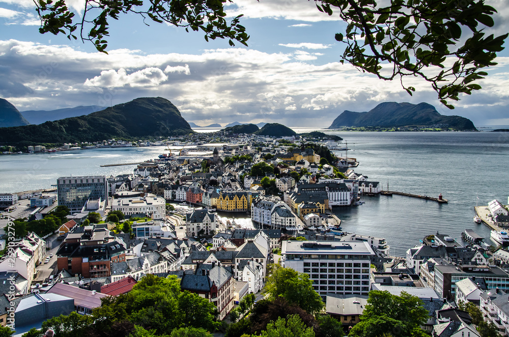 Overview of Alesund town from the Aksla viewpoint during the late evening before sunset with tree leaves framing