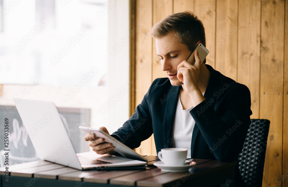 Young handsome man sitting in office with cup of coffee and working on project connected with modern cyber technologies. Businessman with notebook trying to keep deadline in digital marketing sphere. Young handsome man sitting in office with cup of coffee and working on project connected with modern cyber technologies. Businessman with notebook trying to keep deadline in digital marketing sphere.