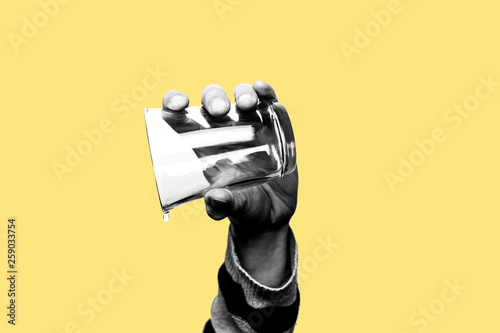 Concept of drought, running out of water, dry summer, global warming. Hand holding an empty glass of water with just one drop falling down. Black and white subject with yellow background