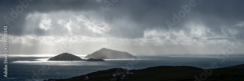 a view of the wild atlantic way off the coast of the ring of kerry in ireland showing skellig michael and surrounding islands in beautiful strong light with cloudy skies 