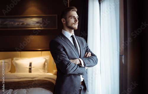Young handsome man relaxing at his apartment in a hotel after business meeting. Business trip. Booking hotel during your vacation. Businessman in luxury room  of the expensive beautiful hotel. 