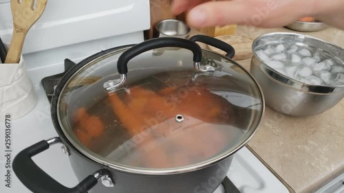Home cooking - Placing glass lid over non stick pot ow boiling or blanching whole and sliced carrots. Ice bath on the right waiting ready to be used to for quick cooling vegetables.