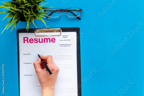 Empoyment concept with resume on blue work desk background with pen, glasses top view photo