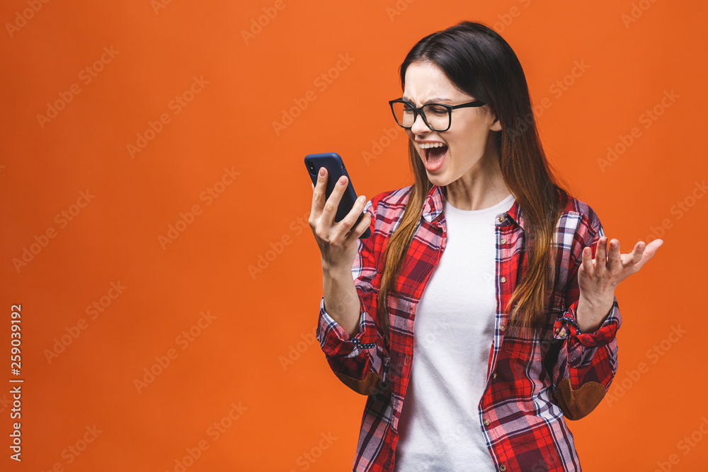 Portrait of an angry young woman shouting at a mobile phone, isolated on a orange background. Portrait of an angry young woman shouting at a mobile phone, isolated on a orange background.