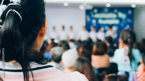 The parent listening and watching student on stage in convention hall.