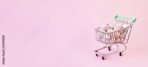 Easter sale concept. Pink Easter eggs in small shopping trolley on pink background.