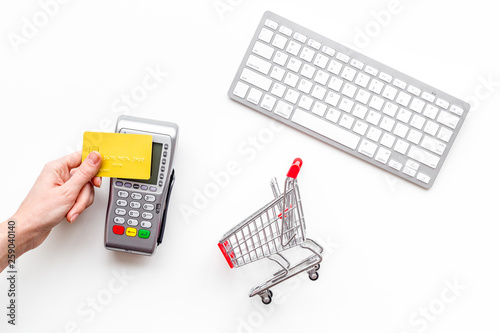 Online shopping concept with trolley near bank card with machine, keyboard on white background top view