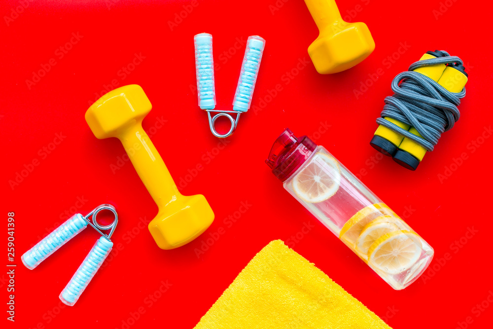 Sport with bars, towel, water and wrist builder red background top view Sport with bars, towel, water and wrist builder red background top view