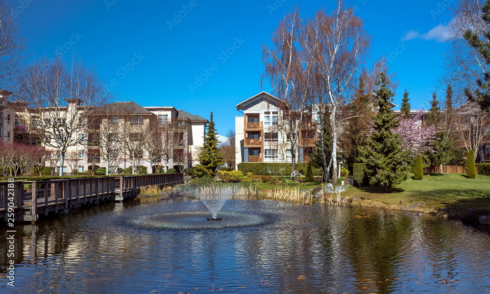 Residential District in Richmond City with pond and fountain, blossom of sakura, green grass bushes and trees in the territory of residential complex, Vanсouver, British Columbia 