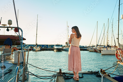 young woman is standing back against the background of beautiful yachts