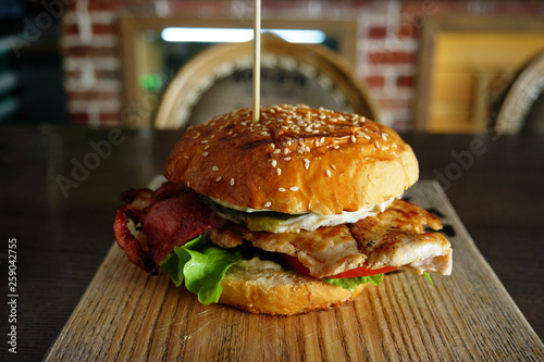 Grilled Burger with backon and salad served on cutting board with blurred pub interior on background photo