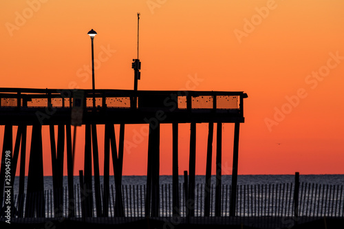 Tall pier agains a beautiful orange and yellow sky just before sunrise. Photo by: Chuck Beyer