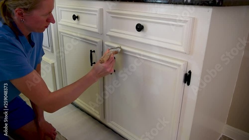 Young blond woman painting a white kitchen cabinet, renovation house work 