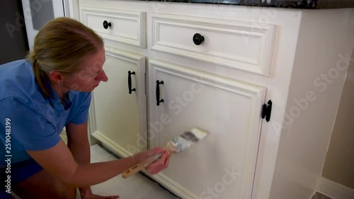 Young blond woman painting a white kitchen cabinet, renovation house work 