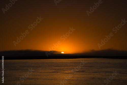 Sun rise from an island in Magdalena bay Baja mexico with a mild fog bank smooth water and violet sand.  