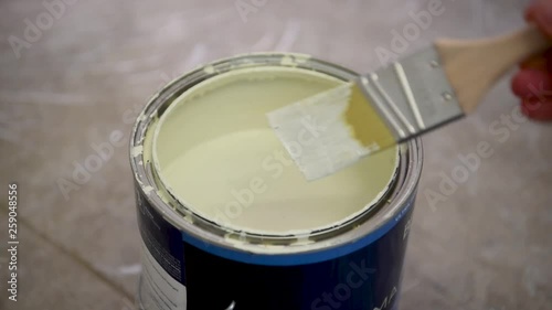 Close-up of woman hand dipping a brush into a white yellow paint color in a paint can