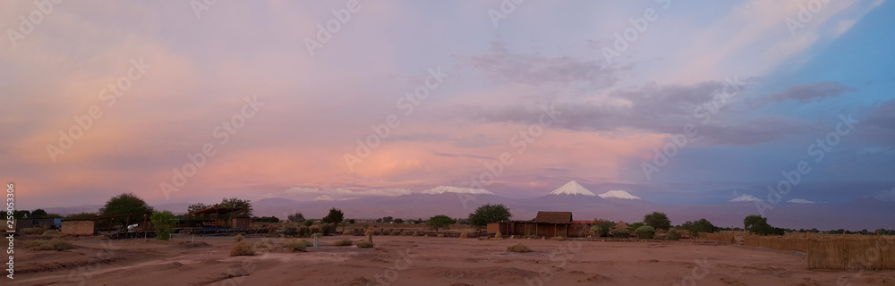 Sunset lights in the arid and desolate landscape of the Atacama Desert and the peaks of the snowy volcanoes of the Andes cordillera in the background