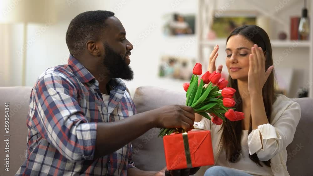 Black man presenting tulips and gift box to his girlfriend, holiday celebration Black man presenting tulips and gift box to his girlfriend, holiday celebration