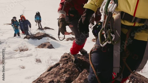Teammate holds out his hand climbing up the side of the mountain climber, helping him to climb up