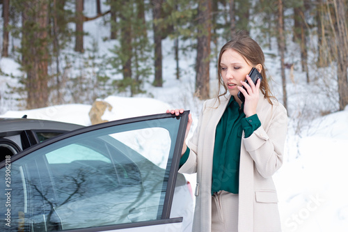 Young businesswoman is speaking on a phone outside of her car